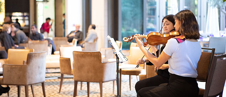Two students play violins at a performance in the lobby