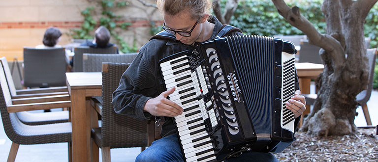 A student plays his accordion beneath a heritage olive tree
